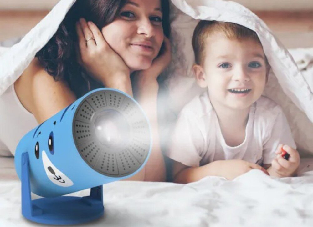 Projektor KIANO Kid Dog wspólne oglądanie filmy rodzina seans, projektor po skosie stojący na białej powierzchni, rodzic z dzieckiem leżący pod kołdrą