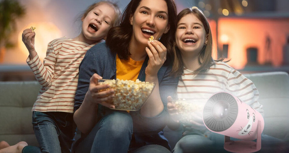 Projektor KIANO Kid Cat kompaktowy mały rozmiar duża projekcja, projektor po skosie, rodzina siedząca na kanapie zajadająca popcorn