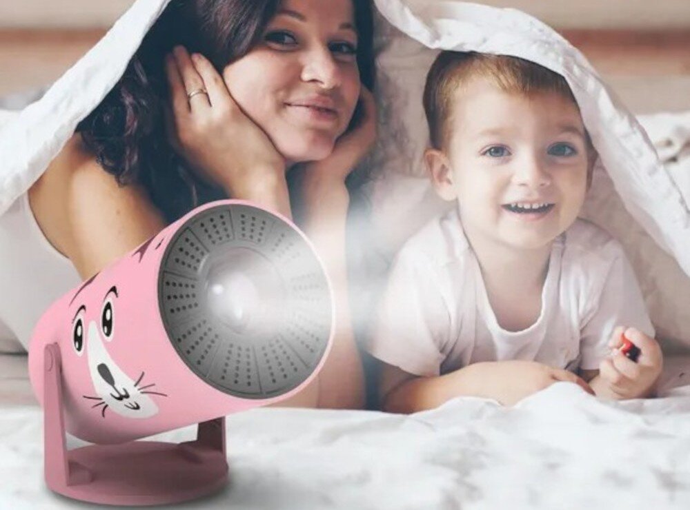 Projektor KIANO Kid Cat wspólne oglądanie filmy rodzina seans, projektor po skosie stojący na białej powierzchni, rodzic z dzieckiem leżący pod kołdrą