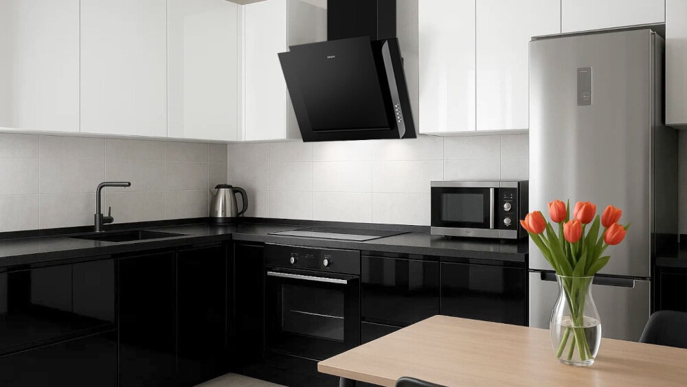 OKAP AKPO WK-4 Grand 50 Na zdjęciu 1.jpg przedstawiono kuchnię w czarno‑białej zabudowie z czarnym, szklanym okapem skośnym zawieszonym nad płytą grzewczą i piekarnikiem do zabudowy. Po prawej stronie widać lodówkę w kolorze inox oraz stół z wazonem czerwonych tulipanów, co dodaje aranżacji przytulnego charakteru