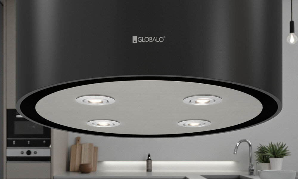 OKAP GLOBALO CYLINDRO ISOLA 39.7 BLACK Zdjęcie przedstawia okap kuchenny w kształcie czarnej tuby firmy Globalo, widziany od dołu. Na spodzie urządzenia znajdują się cztery wbudowane lampki LED rozmieszczone symetrycznie. W tle widoczne są elementy kuchni: zlew, rośliny w doniczkach, drewniane deski oraz piekarnik. Kompozycja podkreśla elegancki wygląd, solidne wykonanie i funkcjonalne oświetlenie okapu światło power led 4200k regulacja barwy światła 2900k 6300k oświetlenie kuchenne dopasowanie nastroju okap oświetlenie robocze oświetlenie