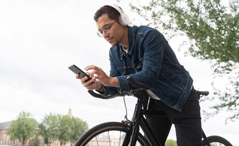 Słuchawki JBL Tune 530BT dwa mikrofony rozmowy wyraźny głos, osoba opierająca się o rower z założonymi słuchawkami nausznymi z telefonem w ręku