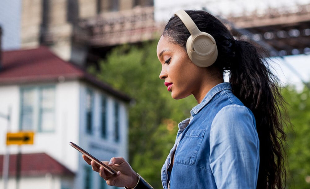 Słuchawki JBL Tune 730BT z mikrofonami do wyraźnych rozmów, osoba z załozonymi słuchawkami nausznymi trzymająca smartfona w ręku