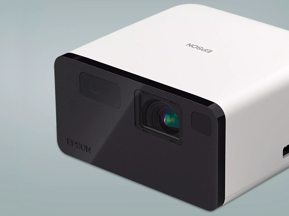 Projektor EPSON EF-21W Projektor na jasnym tle: urządzenie sfotografowane z nieco wyższego kąta, uwidaczniające obudowę, głośniki, dźwięk, łączność Bluetooth