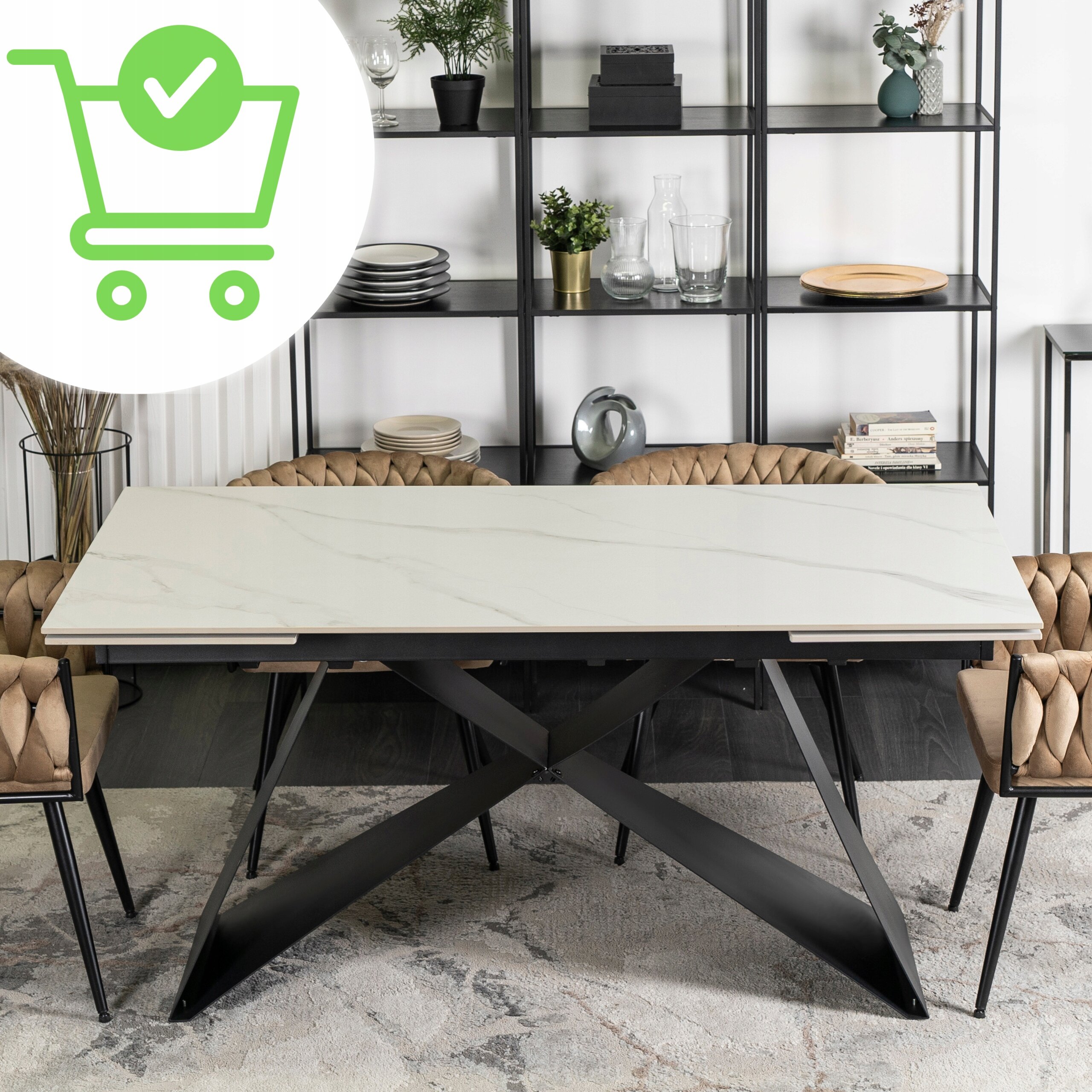 Na obrazie widoczny jest rozkładany stół z białym ceramicznym blatem i czarnymi, krzyżującymi się nogami. W tle znajdują się półki z dekoracjami i naczyniami, a po bokach stołu ustawione są krzesła z jasnobrązowym obiciem.