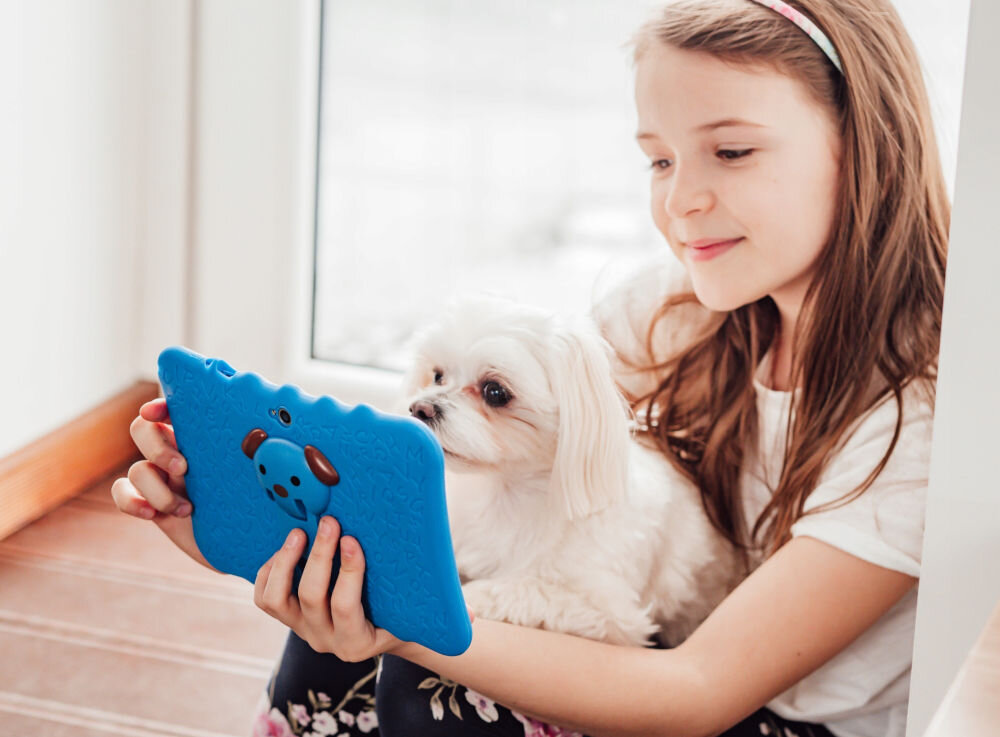 Tablet BLOW Kids Tab 7 V2 7 cali 4/32 GB Wi-Fi Niebieski prezentacja urządzenia dziewczynka trzymająca tablet w pokoju dziennym na kolanach siedzi jej pies