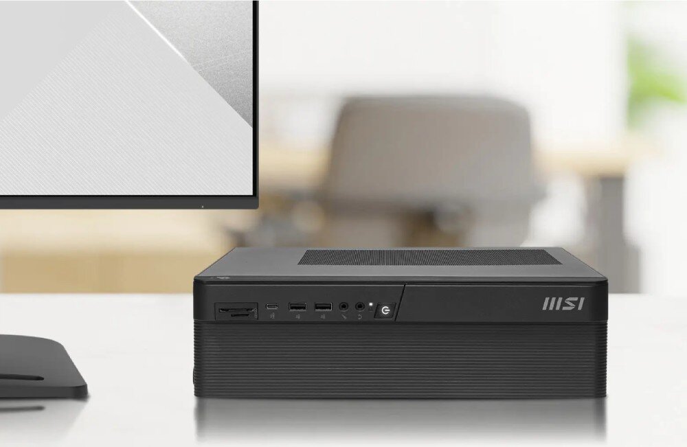 Komputer MSI Pro DP80 A14G-088EU Czarna obudowa komputera leży poziomo na białym blacie biurka. Obok znajduje się fragment monitora oraz rozmyte tło biurowe z fotelem, konstrukcja, wielkość