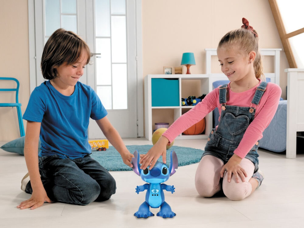 Interaktywny Robot zdalnie sterowany LEXIBOOK Disney Stitch STITCHI17 dwujęzyczny z pilotem w kształcie deski surfingowej sterowanie gestami zabawka edukacyjna Disney Dziewczynka i chłopiec klęczą na dywanie w pokoju dziecięcym, bawiąc się interaktywnym robotem Stichem. Dziewczynka dotyka uszu robota. Oboje uśmiechają się i patrzą na zabawkę. W tle widoczne są meble, w tym biały regał i łóżko.