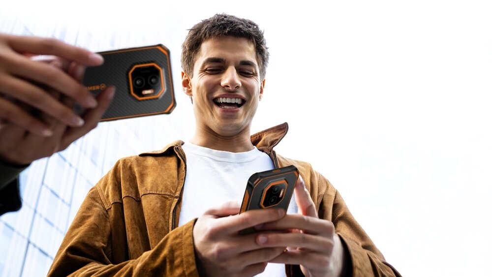 HAMMER ENERGY X2 - tył smartfona na biurku obok laptopa, notesu i okularów; czarno-pomarańczowa, wzmocniona obudowa.