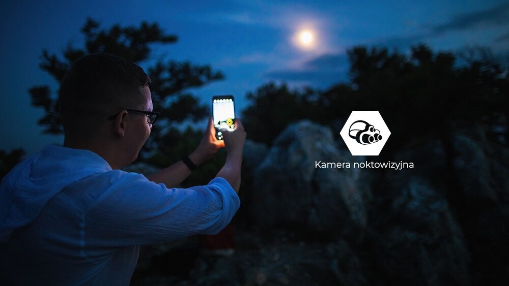 HAMMER ENERGY X2 - postać w ciemnym zaułku, ekran smartfona pokazuje obraz w podczerwieni z kamery noktowizyjnej; ikona noktowizji.