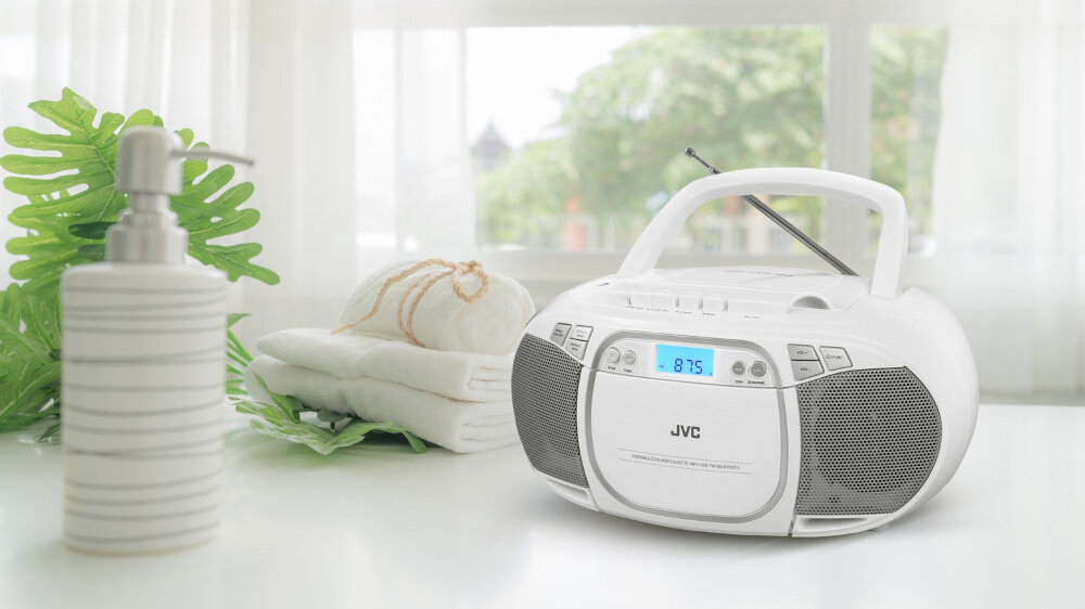 Na białym stole stoi biały radioodtwarzacz z wyświetlaczem pokazującym \'87.5\'. Obok znajdują się złożone ręczniki i dozownik na mydło.