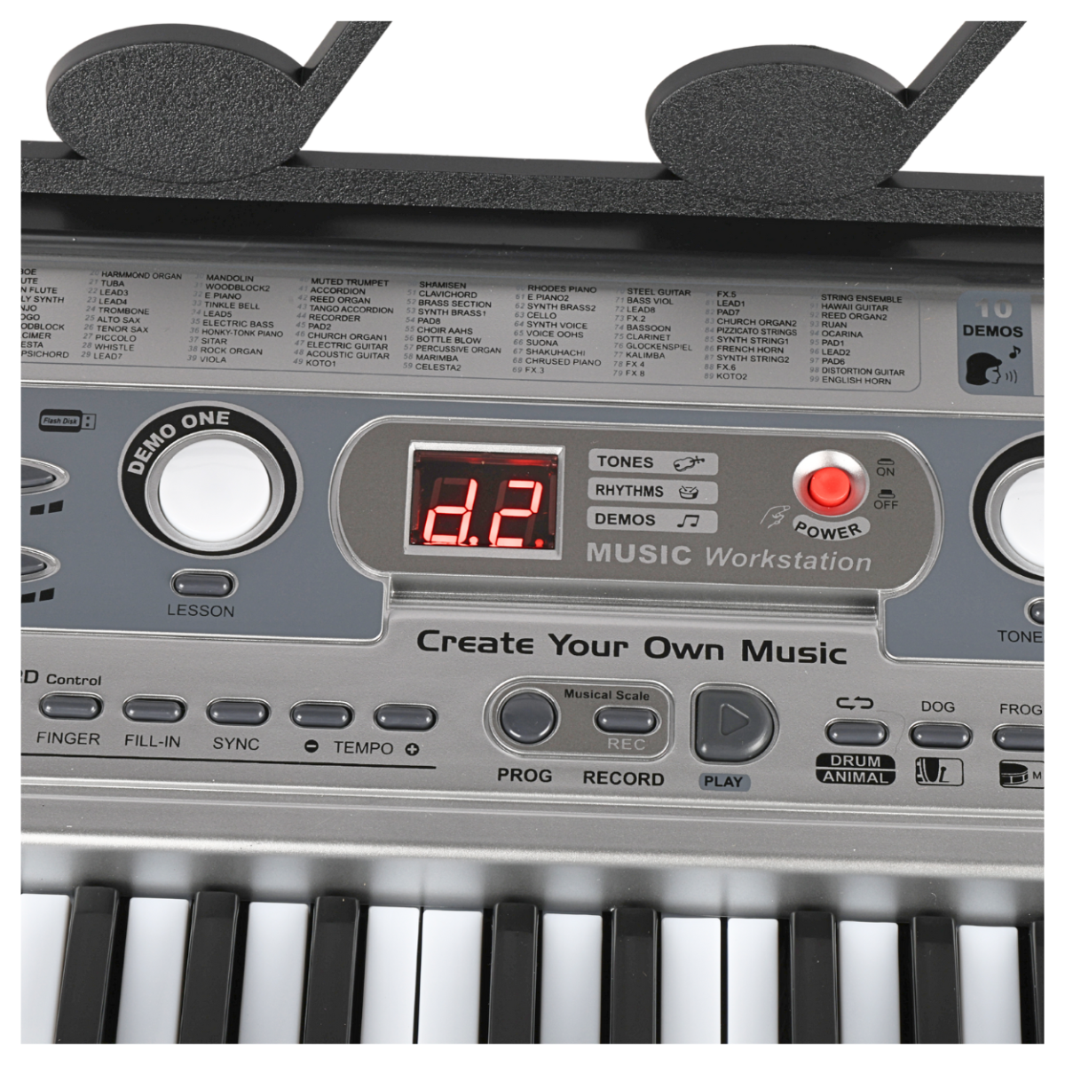 Panel sterowania keyboardu z wyświetlaczem LED pokazującym \'d2\' oraz przyciskami do wyboru tonów, rytmów i dem. Widoczne są napisy: \'Create Your Own Music\', \'MUSIC Workstation\', \'DEMO ONE\', \'POWER\', \'PROG\', \'RECORD\', \'PLAY\'.