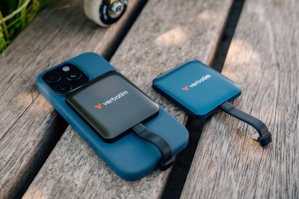 Dysk VERBATIM SnapBack Na drewnianej ławce leży smartfon w etui z dyskiem Verbatim oraz drugi dysk z krótkim kablem; w tle widać koła deskorolki, mocowanie magnetyczne, prędkość, interfejs