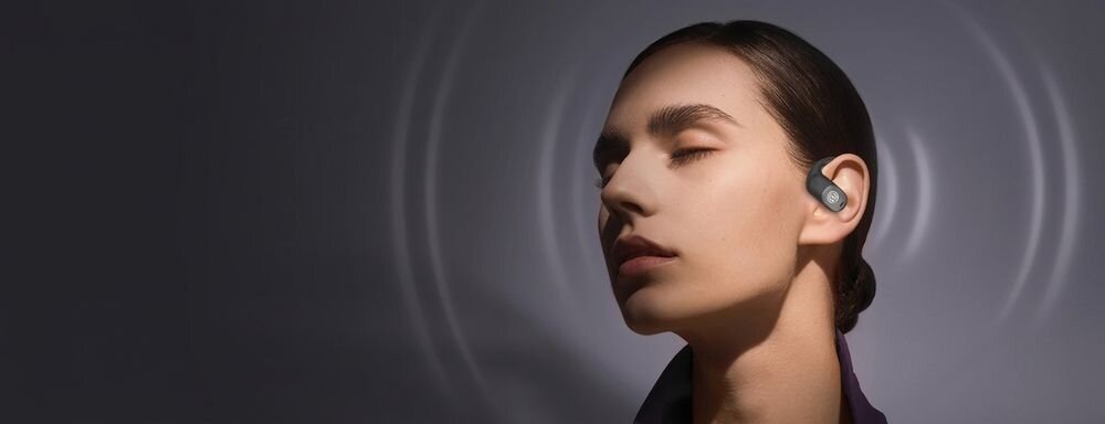 Osoba z zamkniętymi oczami nosi słuchawkę w uchu, a w tle widoczne są koncentryczne fale dźwiękowe.