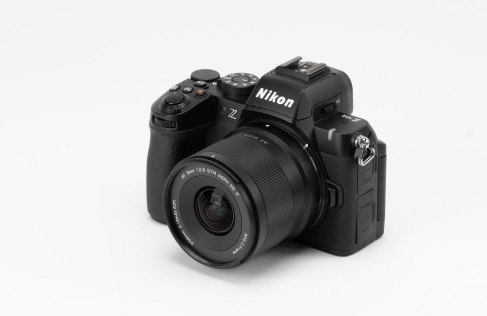 Aparat fotograficzny z obiektywem, na którym widoczny jest napis \'9mm f/2.8 STM ASPH\'. Na korpusie aparatu znajduje się logo \'Nikon\'.