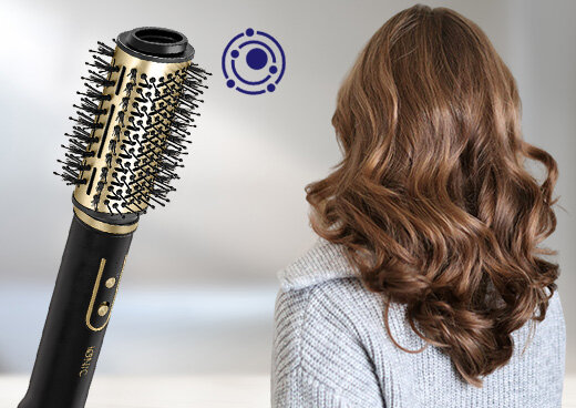 Suszarko-lokówka z uproszczonym symbolem jonizacji. Obok zwrócona tyłem kobieta z długimi włosami.