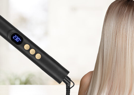 Zbliżenie na przyciska i wyświetlacz na prostownicy. Obok zwrócona tyłem kobieta z długimi włosami.