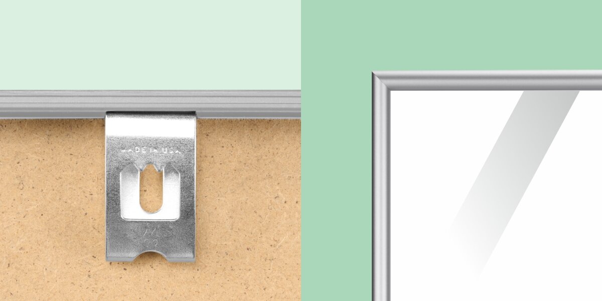 Zbliżenie na tylną część ramy na dokumenty, pokazujące srebrny, metalowy hak (wieszak) z ząbkami, przeznaczony do zawieszania na listwie lub gwoździu, osadzony na płycie pilśniowej. Po prawej widoczny jest fragment srebrnej, metalowej ramy z błyszczącą szybą. Detal pokazuje sposób montażu.