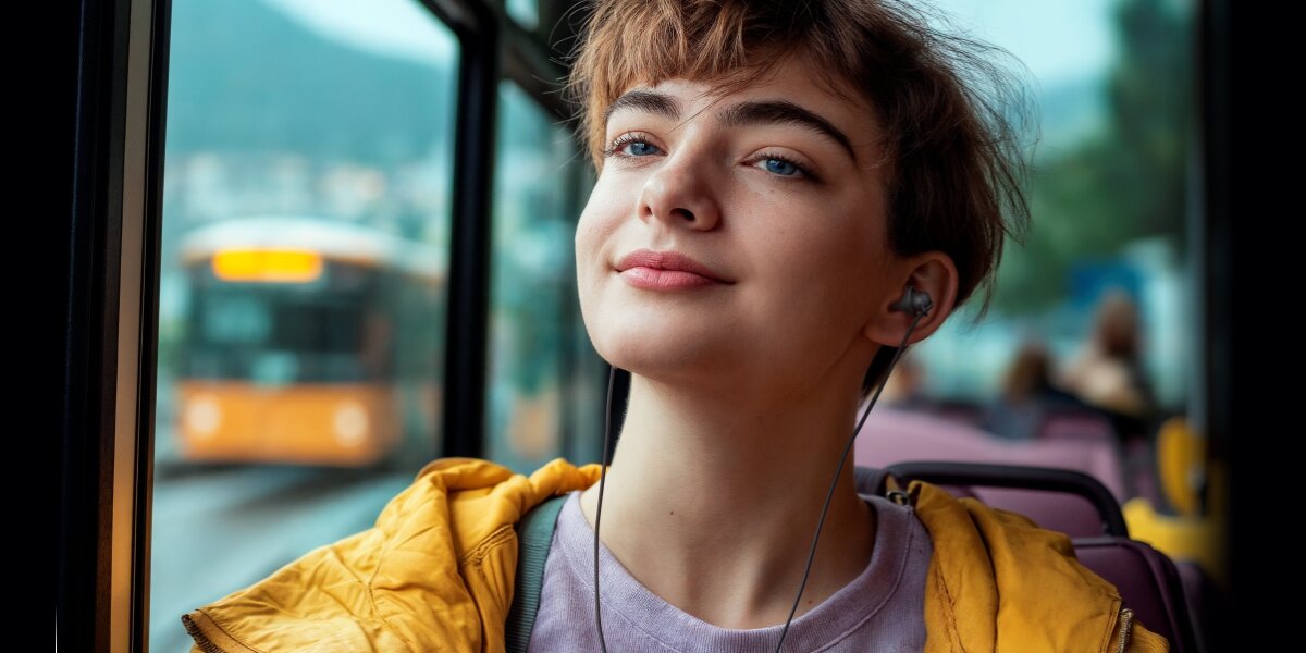 Słuchawki dokanałowe HAMA Relax Czarny Zadowolona młoda osoba w żółtej kurtce słuchająca muzyki przez czarne słuchawki dokanałowe podczas podróży autobusem miejskim.