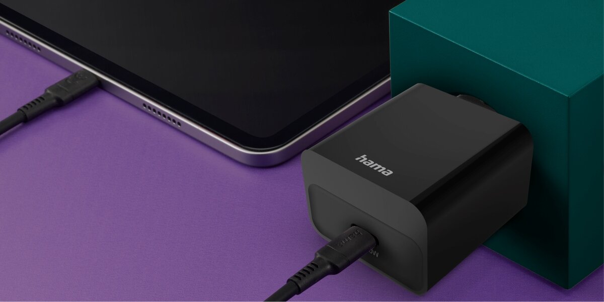 Ładowarka sieciowa HAMA Power Delivery 20W Czarna ładowarka sieciowa Hama wpięta do gniazdka w zielonej ścianie, ładująca tablet za pomocą kabla USB-C. 