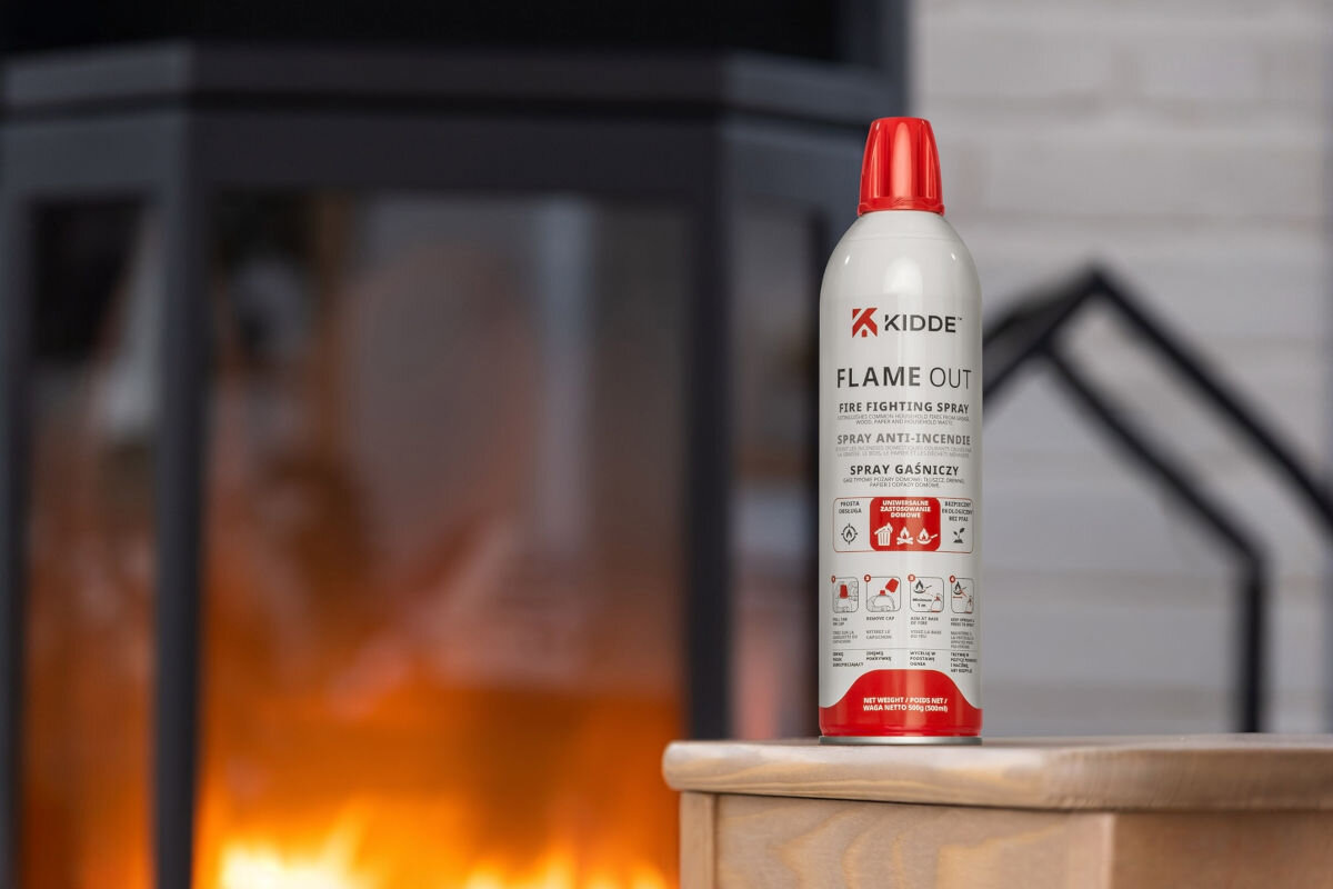 SPRAY GAŚNICZY KIDDE FLAMEOUT (500 ML), pożar, ogień, gaszenie, bezpieczeństwo, Spray gaśniczy Kidde FlameOut ustawiony na drewnianym blacie przy rozpalonym kominku w tle.