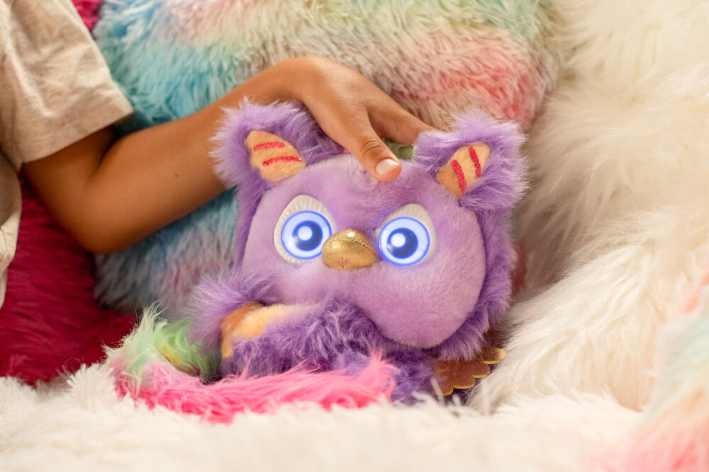 Zabawka interaktywna FURLINGS Furlittles Curiously Cute Gryffin 26117 Zbliżenie na fioletową maskotkę Furlittles Gryffin o podświetlanych niebieskich oczach, trzymaną w dłoni dziecka. Tło to puszysty, tęczowy kocyk.