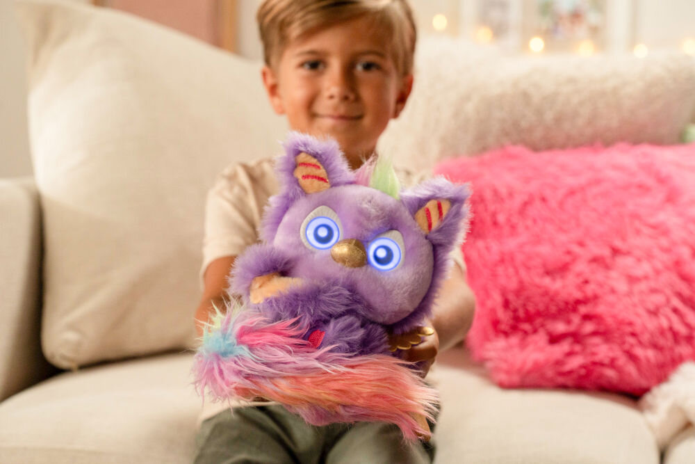 Zabawka interaktywna FURLINGS Furlittles Curiously Cute Gryffin 26117 Uśmiechnięte dziecko trzyma oburącz pluszowego Furlings Furlittles Gryffin, który ma podświetlane, niebieskie oczy.