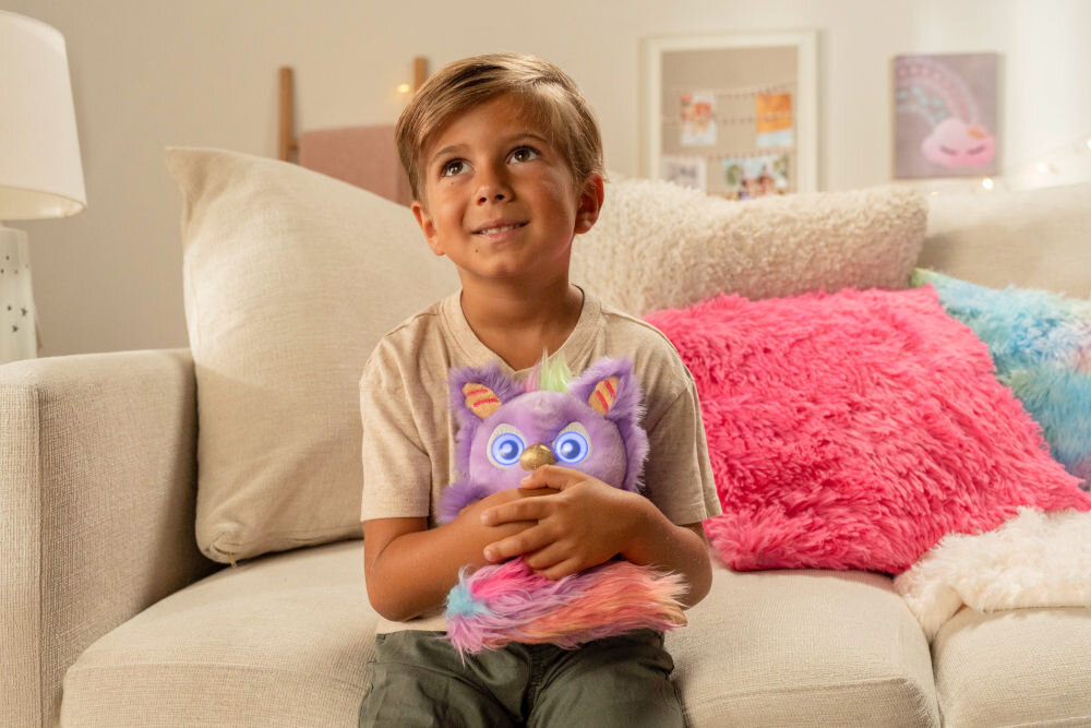 Zabawka interaktywna FURLINGS Furlittles Curiously Cute Gryffin 26117 Szczęśliwe dziecko przytula pluszową maskotkę Furlittles Gryffin w salonie, na kanapie pełnej kolorowych i puszystych poduszek.