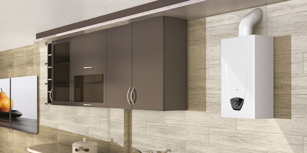 PODGRZEWACZ PRZEPŁYWOWY GAZOWY ARISTON FAST EVO Na zdjęciu widoczne z jasnymi panelami na ścianie, szafkami w ciemnych szarościach oraz białym podgrzewaczem wody ARISTON zamontowanym po prawej stronie. Urządzenie posiada wysystający przewód kominowy od góry, a pod nim widoczny jest panel sterowania z pokrętłem. W części zdjęcia można zobaczyć fragment zlewu oraz garnek ustawiony na blacie roboczym wygląd styl Kompaktowe wymiary
