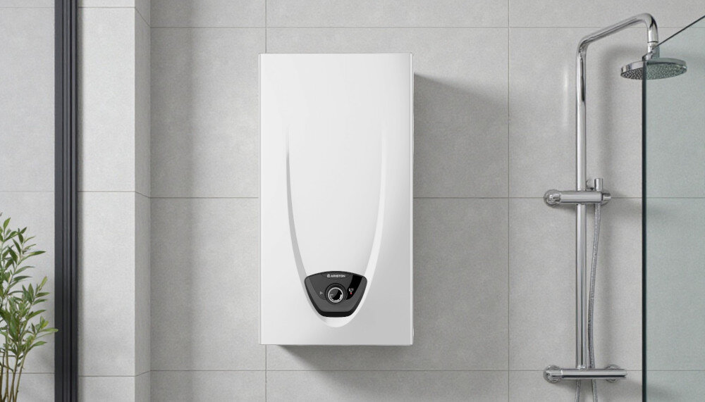 PODGRZEWACZ PRZEPŁYWOWY GAZOWY ARISTON FAST EVO Biały podgrzewacz wody marki Ariston zamontowany na ścianie z jasnoszarą płytką. Po prawej stronie znajduje się chromowana bateria prysznicowa z deszczownicą oraz fragmenty szklanych kabin. W lewym dolnym rogu pojawia się zielona roślina dodawana do świeżości wysoka klasa Elektroniczne sterowanie modeulacja palnika szybkie podgrzewanie