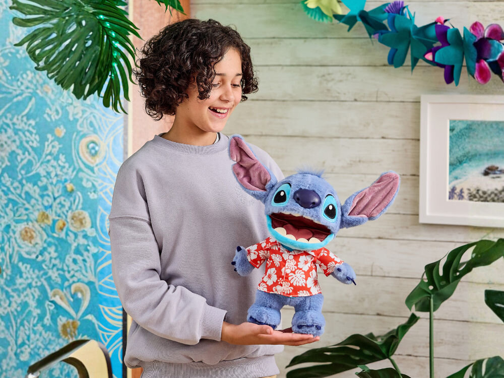 Zabawka interaktywna WOW Disney Aloha Stitch DIS-1027-01 Uśmiechnięte dziecko trzyma na dłoniach małą, interaktywną maskotkę Disney Stitcha w koszuli hawajskiej. Tło w stylu hawajskim/tropikalnym.