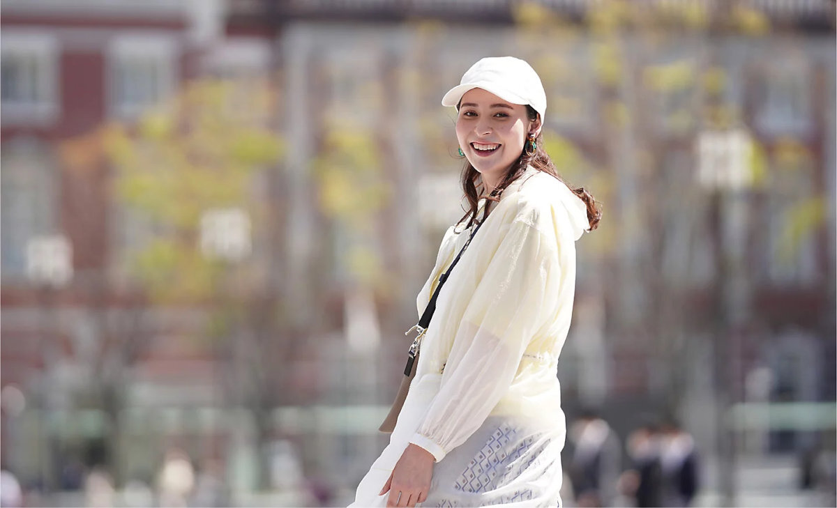 SONY ZV-E10LBD wbudowanemu kierunkowemu mikrofonowi z trzema kapsułami osłonę przeciwwiatrową zewnętrzny mikrofon przez gniazdo 3,5 mm złącze Multi Interface Shoe firmy Sony - Osoba w jasnej kurtce i czapce spaceruje po mieście na tle rozmytych budynków