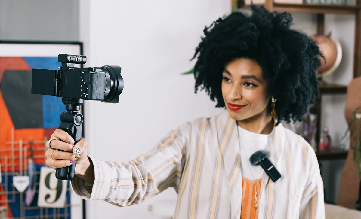 SONY ZV-E10LBD ZV-E10 złącza USB-C transmisje na żywo w jakości Full HD bez potrzeby używania karty przechwytującej aplikacji Sony Imaging Edge łączności Wi-Fi telefon - Kobieta nagrywająca vlog za pomocą aparatu bezlusterkowego na statywie w domowym wnętrzu
