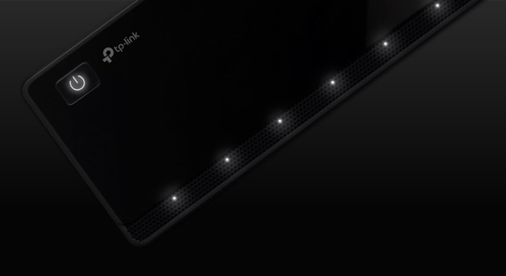 Hub TP-LINK UH700 Zbliżenie na górną część czarnego urządzenia w ciemnym otoczeniu z podświetlonym przyciskiem zasilania oraz rzędem białych diod kontrolnych