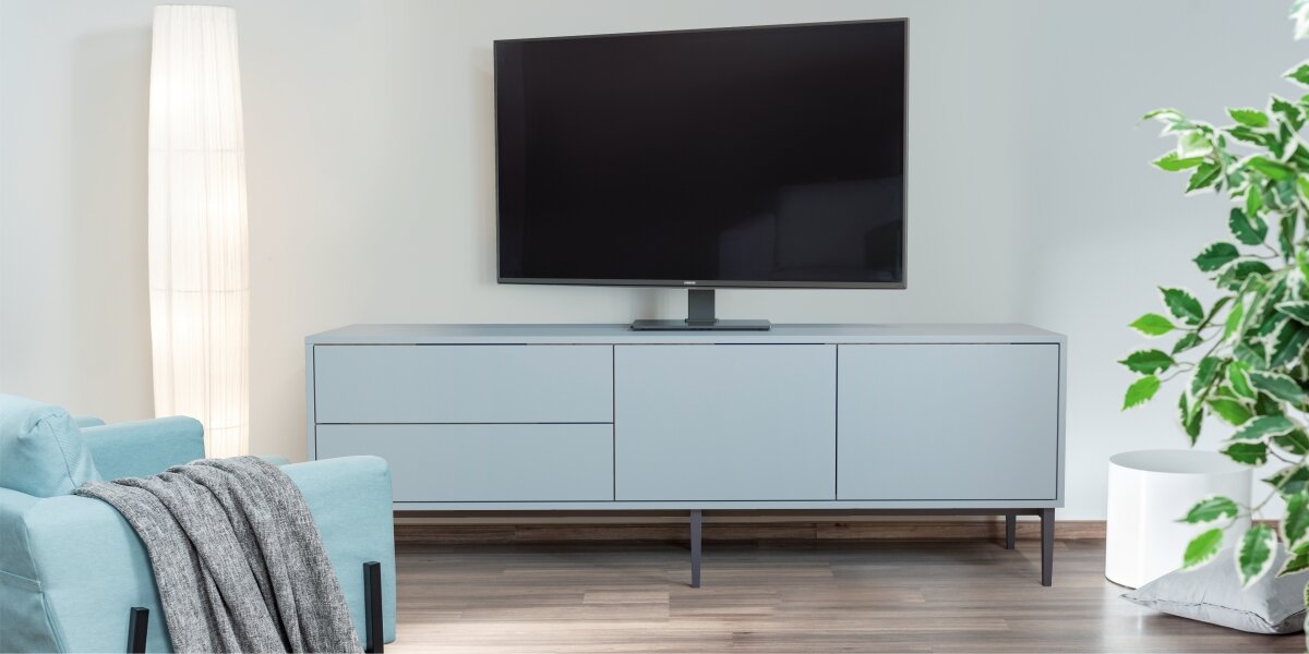 Stojak podłogowy HAMA do TV 32-65 cali 220867 Czarny Telewizor na stabilnej, czarnej podstawie Hama ustawiony na niskiej szafce RTV w nowoczesnym, minimalistycznym wnętrzu.