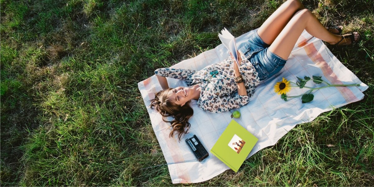 Album HAMA Fine Art Jumbo Białe kartki Zielony (100 stron) Kobieta relaksująca się na kocu na trawie, oglądająca zielony album na zdjęcia w słoneczny dzień podczas pikniku.