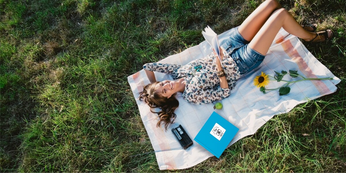 Album HAMA Fine Art Jumbo Białe kartki Błękitny (100 stron) Kobieta relaksująca się na kocu na trawie, oglądająca błękitny album na zdjęcia w słoneczny dzień podczas pikniku.