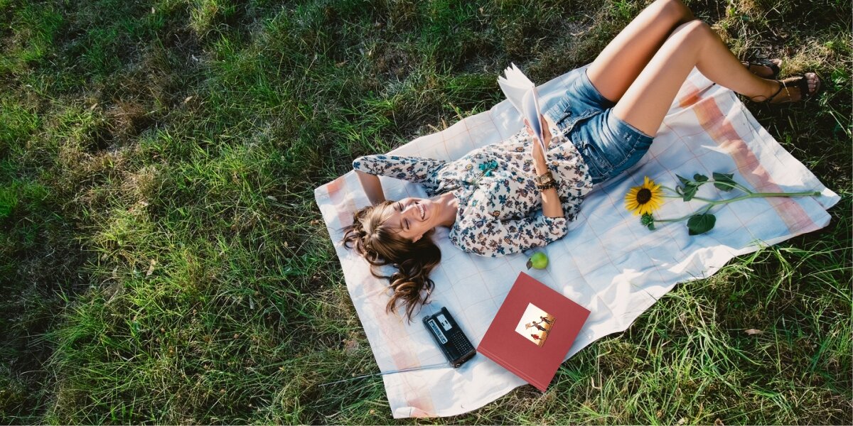 Album HAMA Fine Art Jumbo Białe kartki Bordowy (100 stron) Kobieta relaksująca się na kocu na trawie, oglądająca bordowy album na zdjęcia w słoneczny dzień podczas pikniku.