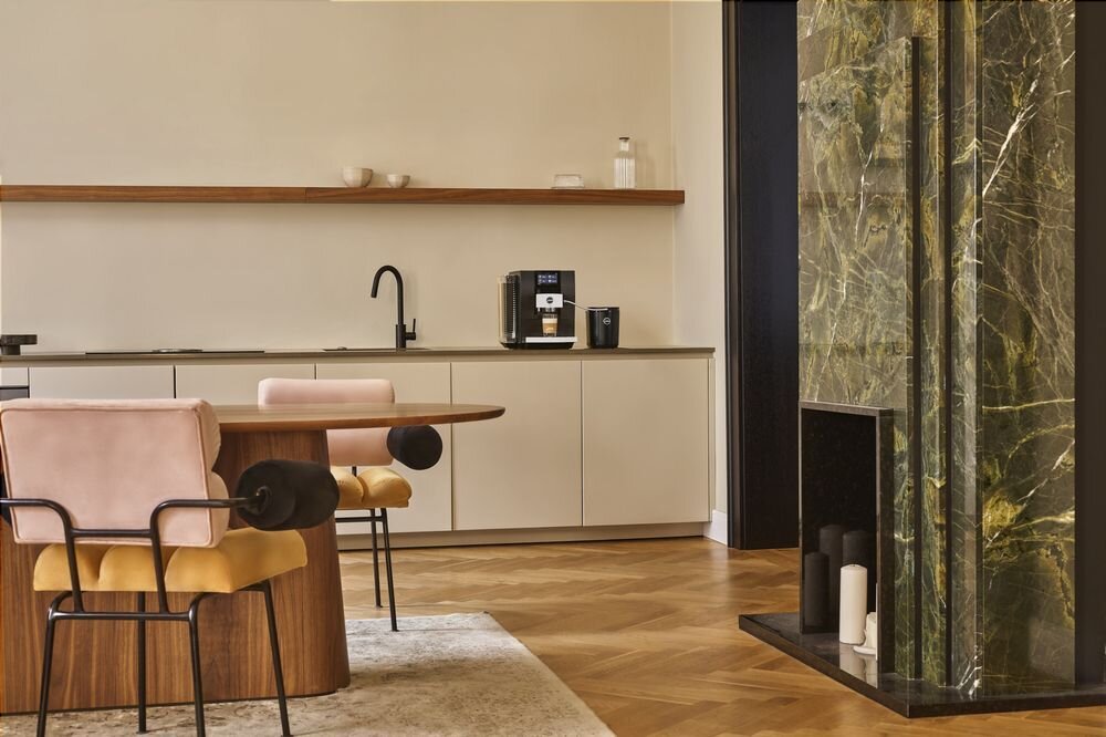 Kuchnia z ekspresem Jura Z10 na blacie, widok na stół z designerskimi krzesłami oraz ozdobną ścianę z zielonego marmuru