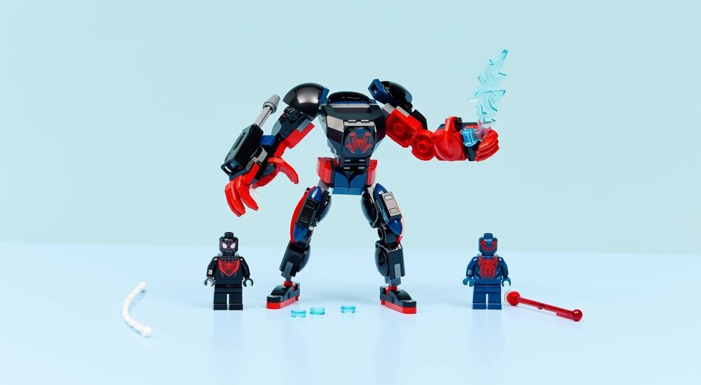 Na jasnoniebieskim tle znajduje się zestaw LEGO z dużą figurką robota oraz dwoma małymi figurkami postaci. Robot ma czerwono-czarne elementy, a obok niego leżą akcesoria LEGO.