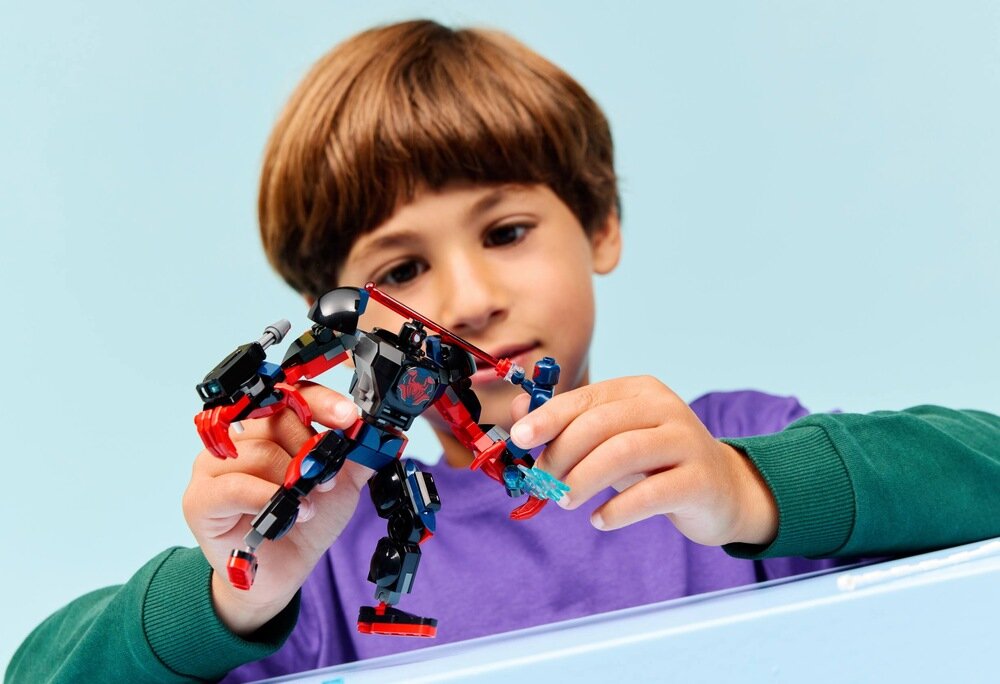 Dziecko bawi się zestawem klocków LEGO przedstawiającym postacie w kolorach czarnym, czerwonym i niebieskim. Tło jest jasnoniebieskie.