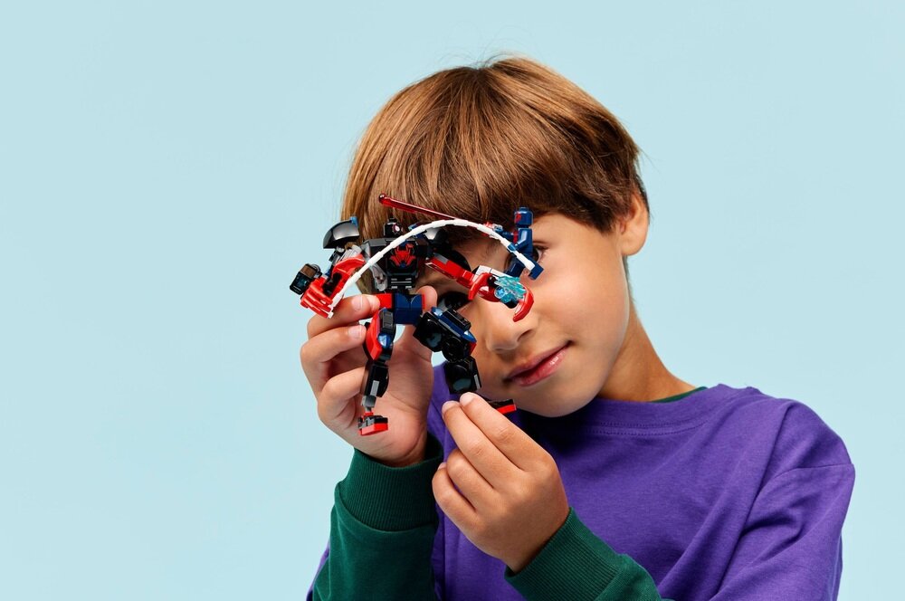 Dziecko trzyma w rękach figurki LEGO przedstawiające postacie superbohaterów. Tło jest jednolite, w jasnym kolorze.