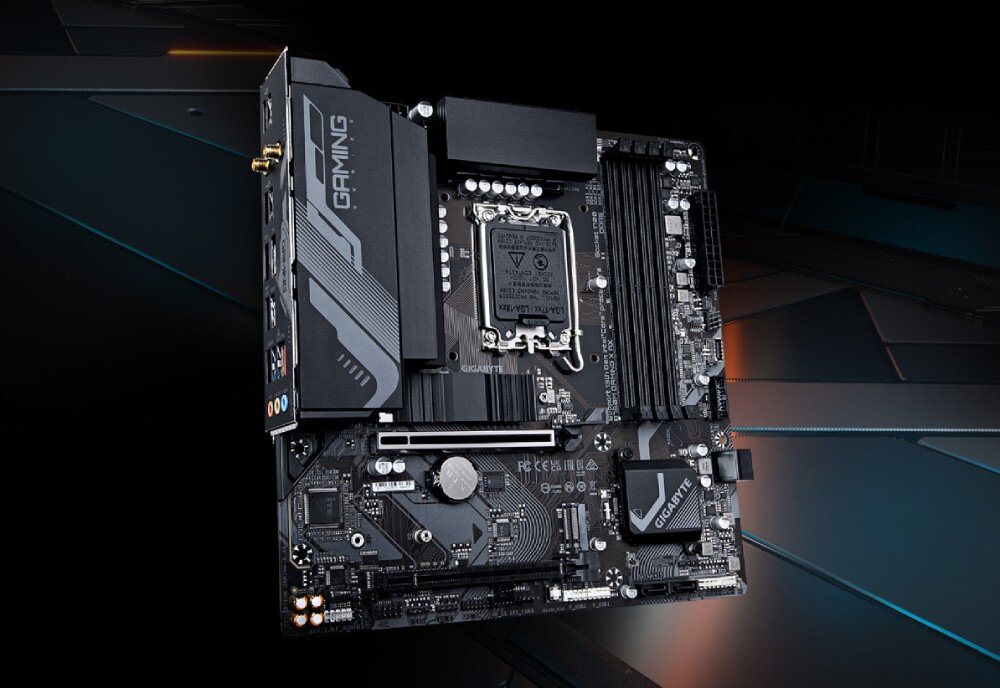 Komputer MAD DOG LOGIC-ARGB-I06WR32WH Ujęcie płyty głównej w czarno-szarej kolorystyce z widocznym gniazdem procesora Intel LGA1700, czterema slotami pamięci RAM, złączem PCIe, radiatorami sekcji zasilania i napisem 'GAMING' na osłonie portów tylnych