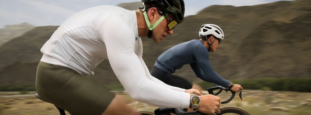 Dwóch rowerzystów jedzie na rowerach w górzystym terenie. Jeden z nich nosi smartwatch na nadgarstku.