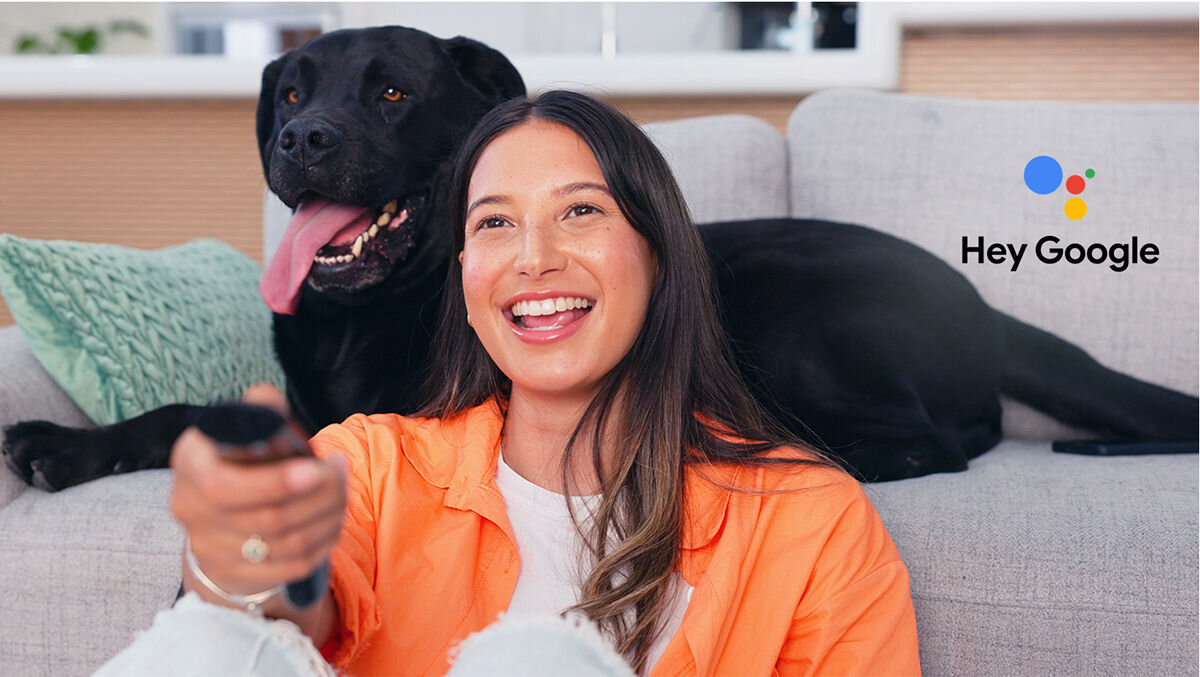 Telewizor SHARP 65HR8765E Asystent Google, sterowanie głosem, szybki dostęp do filmów i seriali, osoba siedząca przed kanapą na podłodze, pies leżący na kanapie