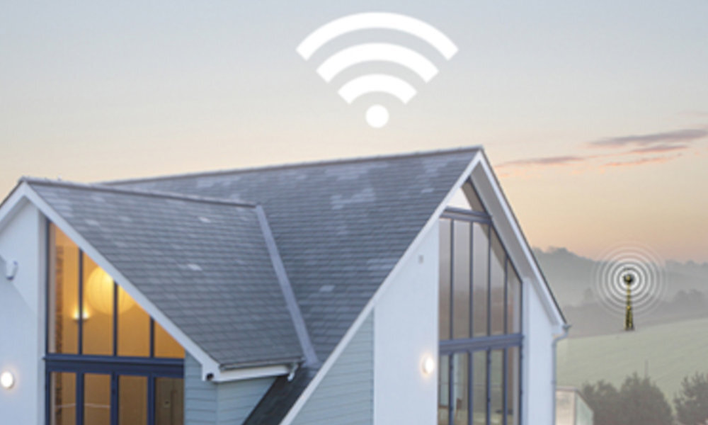 Obraz przedstawia nowoczesny dom z dużymi oknami, nad którym unosi się symbol sygnału Wi-Fi. W tle widoczna jest wieża nadawcza na tle krajobrazu o zmierzchu.
