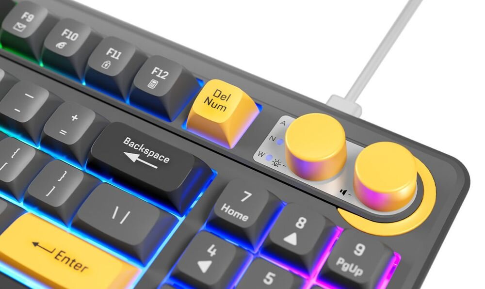 Klawiatura z podświetleniem RGB, posiada żółte klawisze \'Del Num\' i \'Enter\', oraz dwa żółte pokrętła. Widoczne są klawisze funkcyjne i strzałki kierunkowe.