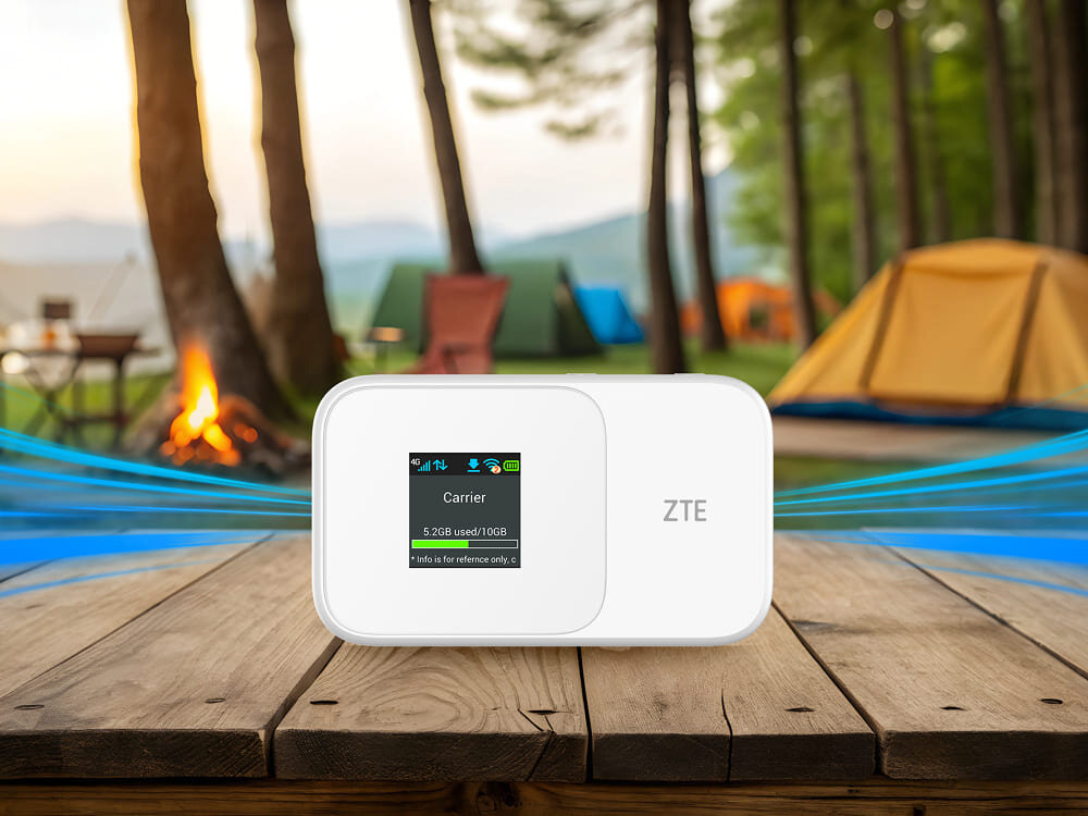 Router ZTE 986D Biały przenośny modem ZTE stoi na drewnianym stole na zewnątrz, ekran wyświetla status połączenia, a wokół widać namioty i ognisko, standard, sieć LTE, prędkość