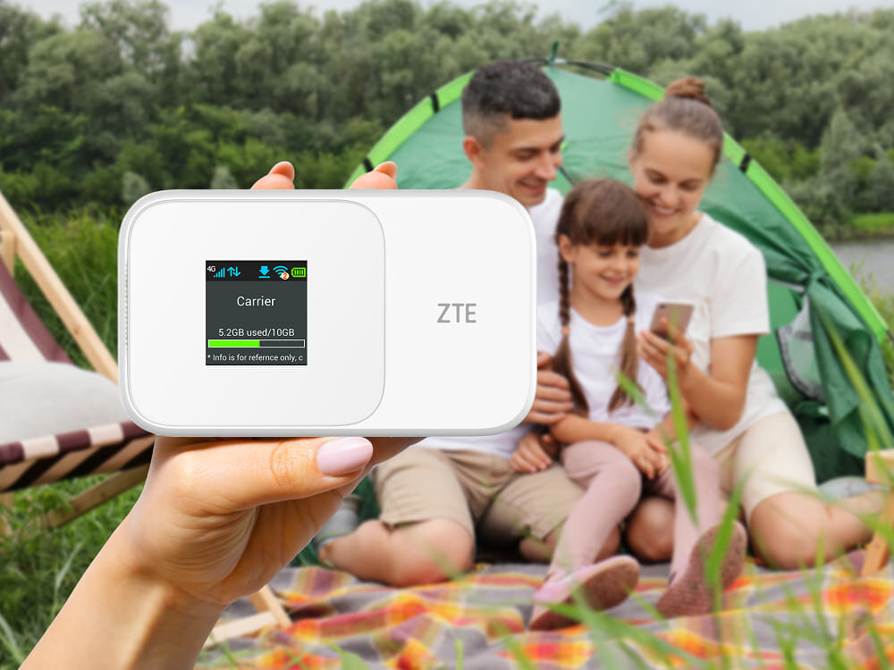 Router ZTE 986D Przenośny hotspot Wi-Fi trzymany w ręku, w tle rodzina korzysta ze smartfonów na kempingu, pokazując mobilną łączność, waga wielkość, port
