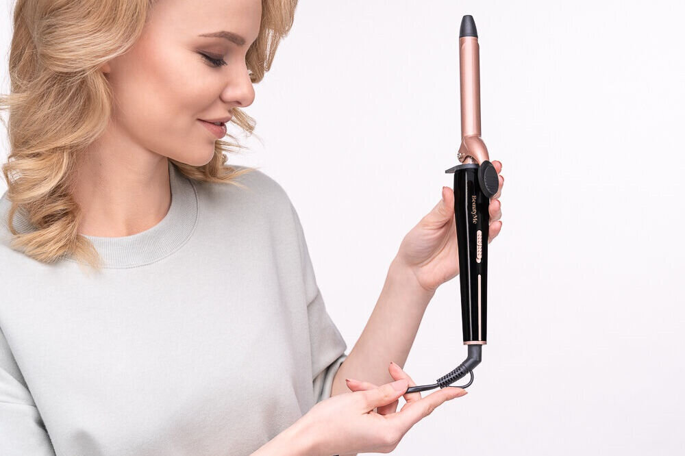 Osoba trzyma lokówkę o metalicznym wykończeniu z czarnym uchwytem. Na uchwycie widoczne jest logo \'BEAUTYME\'.